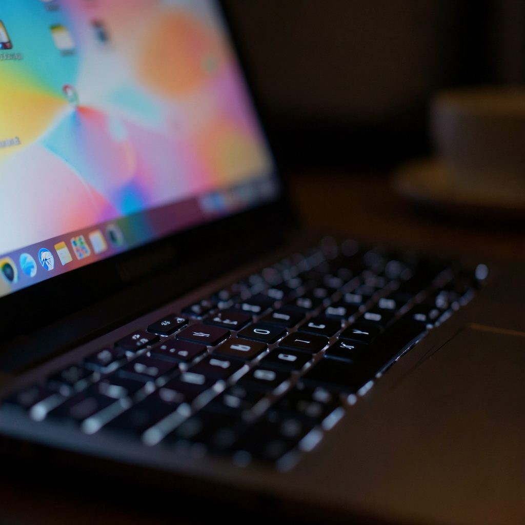 Close-up of a laptop keyboard in low light, faint colorful glow from the display, cozy late-night browsing mood